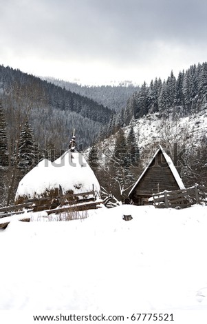 Winter landscape in mountains with an old cottage and haystacks