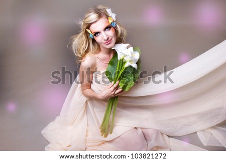 studio portrait of beautiful blonde with blue eyes with  butterfly in her hair and flowers calla
