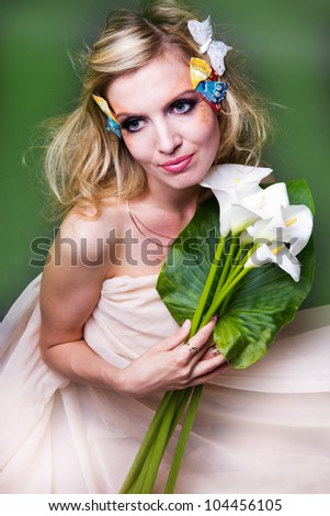 studio portrait of beautiful blonde with blue eyes with butterfly in her hair and flowers calla