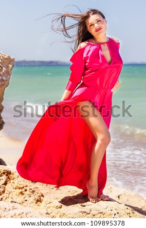 Sexy young woman in long red dress flying under wind