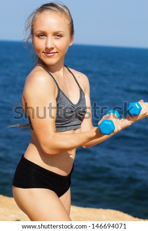 Portrait of healthy young woman in sportswear exercising with hand weights on the beach