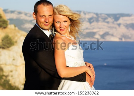 Couple in love young bride and groom dressed in white hugging on cliff background of blue sea