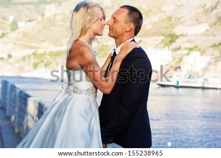 Couple in love young bride and groom dressed in white hugging on cliff background of blue sea