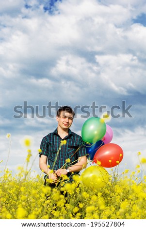Young man in a spring field with lots of balloons
