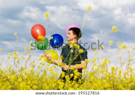 Young man in a spring field with lots of balloons