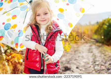 Little girl with umbrella in red vest outdoor