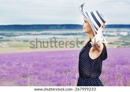 Beautiful girl is wearing stripped hat standing in fairy field of purple lavender. Summer time