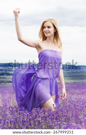 Beautiful blonde girl is wearing purple dress relaxing in fairy field of purple lavender. Summer time