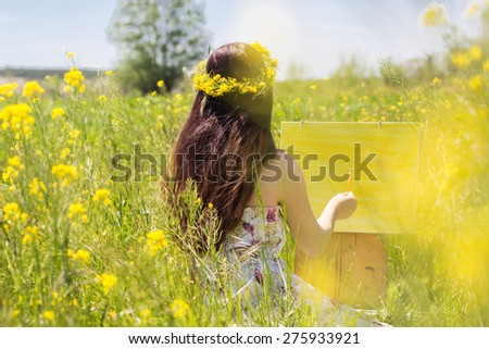 Young female woman is wearing wreath of yellow flowers is painting picture of an floral landscape, spring time