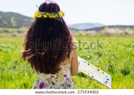 Young female artist is holding palette an floral landscape, summer time