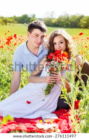 Young happy couple man and woman resting on a green meadow full of poppy flowers