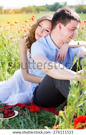 Young happy couple man and woman resting on a green meadow full of poppy flowers