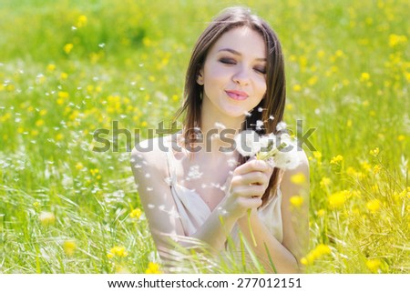 Beautiful girl is holding dandelion in the field of yellow flowers is wearing flying white wedding dress