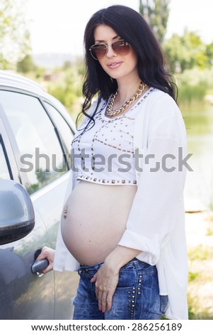 Pregnant brunette girl with big belly near her car