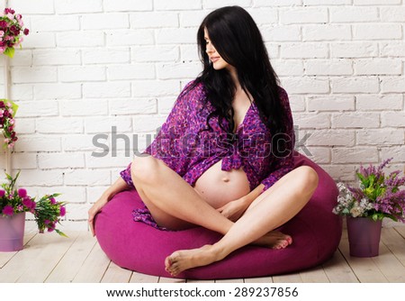 Pregnant smiling girl is wearing sexy underwear sitting on puprle pillow over white background