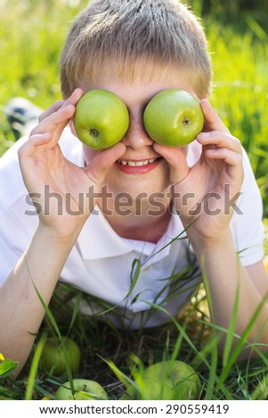 Funny portrait of blonde smiling boy with freckle face on his face is holding two green apples