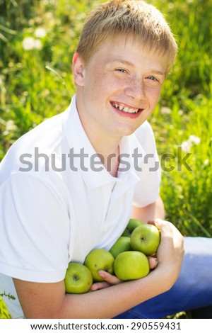 Portrait of cute smiling boy with freckle face on his face is holding two green apples