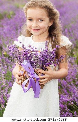 Happy little girl is wearing white dress in a lavender field holding a basket full of flowers