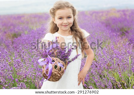 Portrait of pretty cute child girl is resting in a lavender field holding a basket full of purple flowers