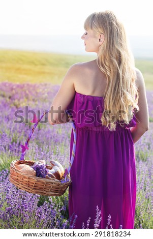 Beautiful pregnant blonde woman is wearing purple dress is holding basket with sweet-stuff