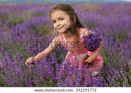 Happy cute little girl is in a lavender field holding bouquet of purple flowers