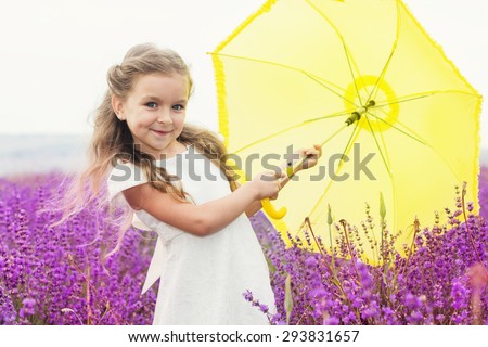 Pretty child girl is in a purple lavender field holding an yellow umbrella