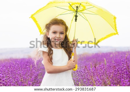 Pretty child girl is in a purple lavender field holds an yellow umbrella