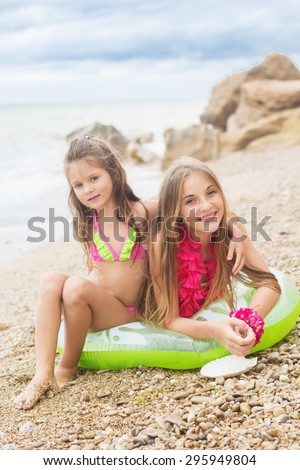 Two pretty smiling sisters are wearing colorful hawaiian flowers and swimsuits sitting on green rubber ring at the beach, summer time
