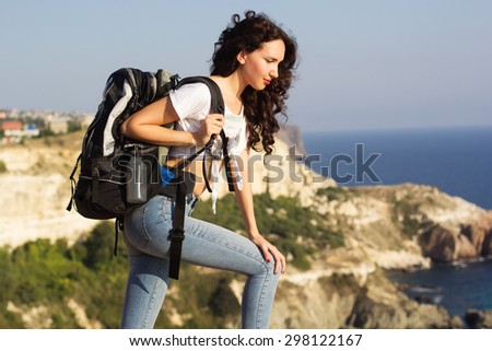 Pretty traveler girl is looking down on rock edge over mountains view with backpack, summer time