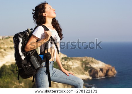 Young pretty slim woman standing with backpack on cliff\'s edge and looking into a wide valley