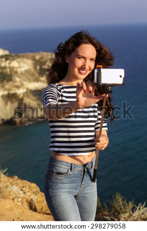 Tourist smiling slim girl making selfie photo with stick on the peak of mountain over sea background