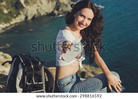 Pretty smiling traveler girl backpacker is drinking water on rock peak over sea view with backpack, summer vacations