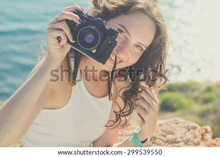 Tourist smiling slim girl making photo by old camera on the peak of mountain over sea background