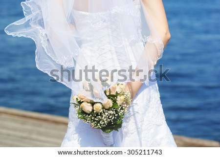Bride in a white dress in summer time over sea background with a bouquet of roses in hands