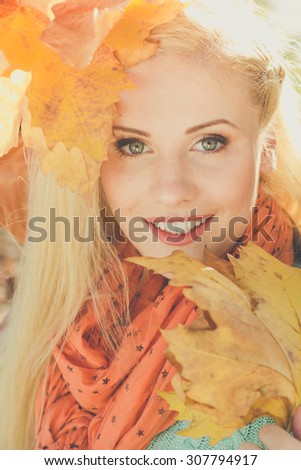Face of young pretty girl in autumn park is holding yellow maple leaves