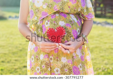 Pregnancy, maternity and new family concept - pregnant woman and heart symbol outdoors in sunny summer day in green park