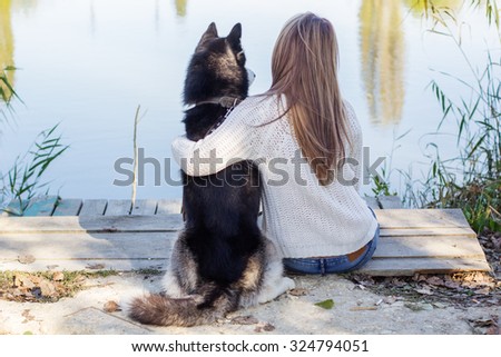 Back view of girl and her blueyed dog husky is sitting outdoors near lake, autumn time