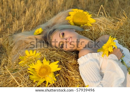 The beautiful girl lies on a haystack with sunflowers