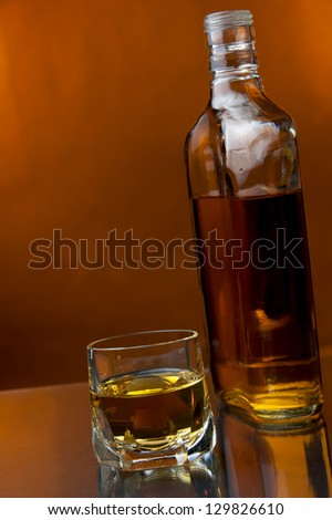 a glass and a bottle of hard liquor at warm backdrop