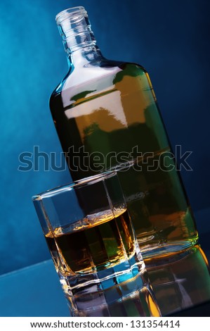 a bottle of whiskey and glass of whiskey against color background