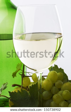 white wine glass and green wine bottle and green grape against white background