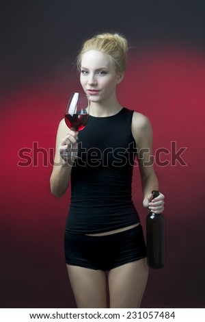 beauty blond model holding wineglass with red wine and wine bottle getting ready to take sip