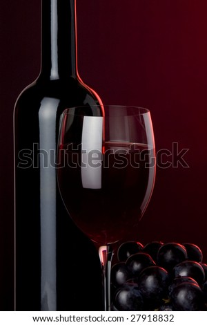 a glass of red wine and a bottle and grape