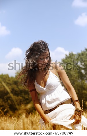 Beautiful woman standing on a wheat field outdoors on a hot summer afternoon. She is wearing a nice white dress and has long brown hair.