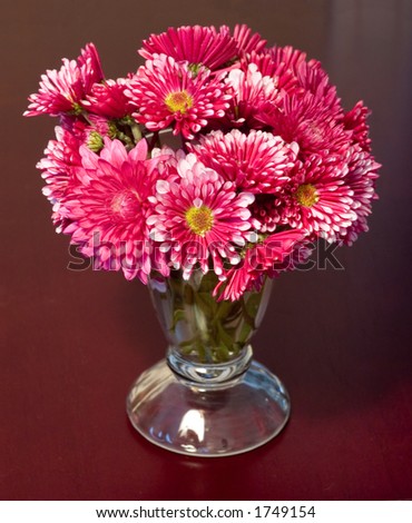 Vase of small red flowers on wood table background.
