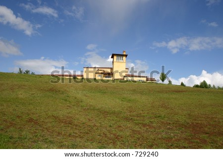 Very large house in the country with blue sky and puffy white clouds on a hill