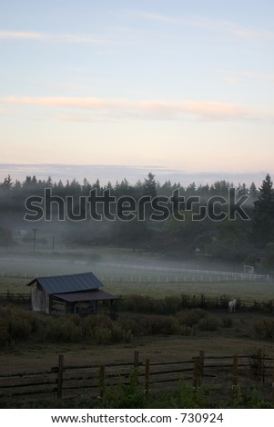 Sunrise on the farm with mist rising from the ground and a barn in the foreground