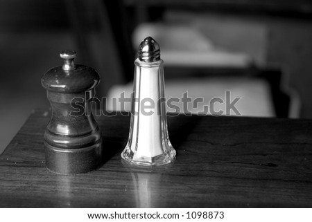 A salt shaker and pepper grinder at a restaurant table in black and white