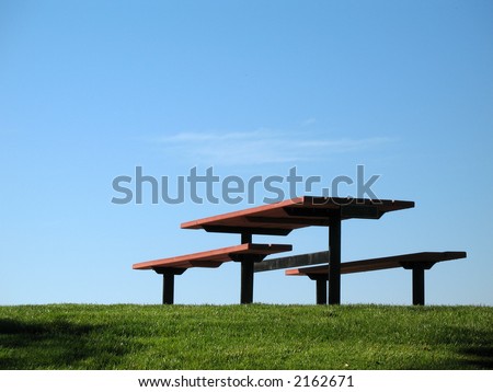 An empty picnic table sits on the green grass and blue sky background