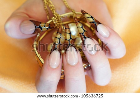 Beautiful female hand with long Decorative French Nail Art Design Stiletto nails holding golden jewelery